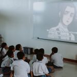 Ilustrasi murid-murid berseragam menonton tayangan dari proyektor di dalam kelas.