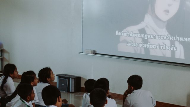 Ilustrasi murid-murid berseragam menonton tayangan dari proyektor di dalam kelas.