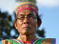 Ledjie Taq, tokoh adat Dayak Wehea, berkacamata dengan topi anyaman dan rompi bermotif
