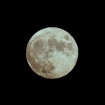 Ilustrasi bulan purnama dengan bercak gelap di permukaannya pada langit malam.