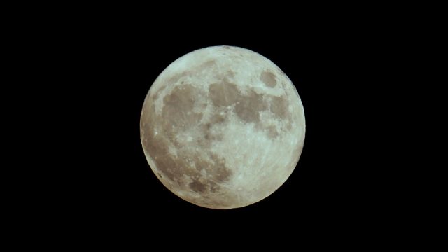 Ilustrasi bulan purnama dengan bercak gelap di permukaannya pada langit malam.