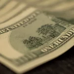 Lembaran uang seratus dolar Amerika Serikat tersusun bertumpuk di permukaan gelap