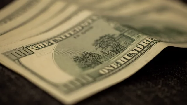 Lembaran uang seratus dolar Amerika Serikat tersusun bertumpuk di permukaan gelap