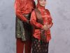 Ilustrasi sepasang orang mengenakan busana songket merah lengkap dengan penutup kepala.