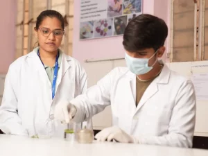 Dua mahasiswa berjas lab putih melakukan praktikum di laboratorium kampus di India