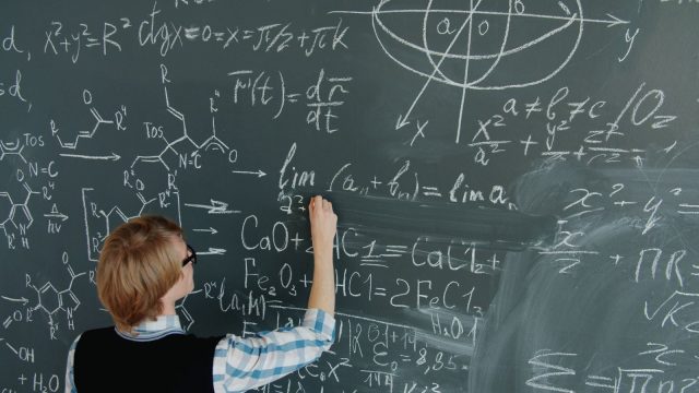 Ilustrasi seorang perempuan menuliskan deretan rumus matematika dengan kapur pada papan tulis hijau yang penuh coretan.