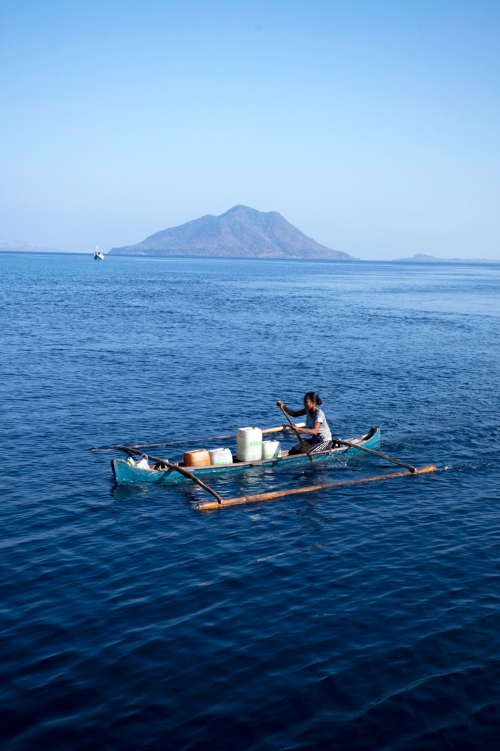Ilustrasi sebuah perahu kecil melintas di laut biru yang luas dengan siluet pulau di kejauhan.