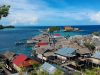 Ilustrasi permukiman rumah panggung beratap seng berdesakan di tepi laut biru di antara batu karang dan pepohonan.