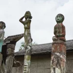 Tiga patung sapundu kayu berdiri di depan rumah Betang Toyoi, Kalimantan