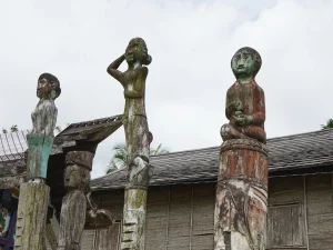 Tiga patung sapundu kayu berdiri di depan rumah Betang Toyoi, Kalimantan