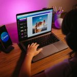 Ilustrasi seorang remaja mengerjakan desain di laptop dengan pencahayaan berwarna.