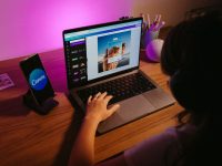 Ilustrasi seorang remaja mengerjakan desain di laptop dengan pencahayaan berwarna.
