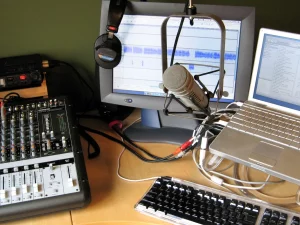Meja studio podcast dengan mixer, mikrofon kondensor, monitor, dan laptop