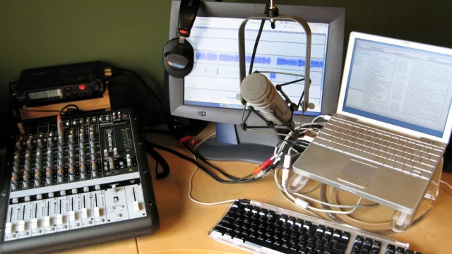 Meja studio podcast dengan mixer, mikrofon kondensor, monitor, dan laptop