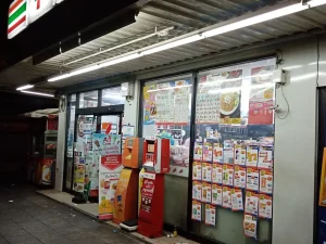 Fasad gerai 7-Eleven dengan mesin ATM pada malam hari di Bang Yi Ruea, Bangkok, Thailand