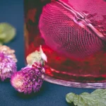 Segelas minuman herbal berwarna merah dihiasi bunga dan daun mint