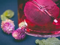 Segelas minuman herbal berwarna merah dihiasi bunga dan daun mint