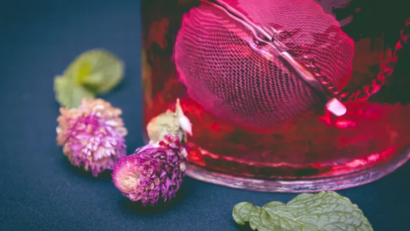 Segelas minuman herbal berwarna merah dihiasi bunga dan daun mint