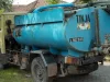Truk tangki biru bertuliskan TINJA dengan selang sedot terparkir di jalan kampung