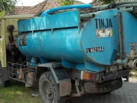 Truk tangki biru bertuliskan TINJA dengan selang sedot terparkir di jalan kampung