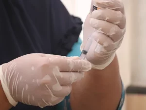 Tangan petugas kesehatan bersarung tangan lateks menyiapkan jarum suntik vaksin dari botol kecil