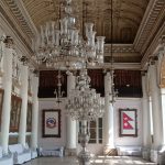 Ilustrasi aula istana bergaya lama dengan deretan lampu gantung kristal.