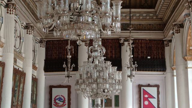 Ilustrasi aula istana bergaya lama dengan deretan lampu gantung kristal.