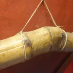 Tabung bambu bergores aksara Ulu digantung dengan tali di depan dinding merah