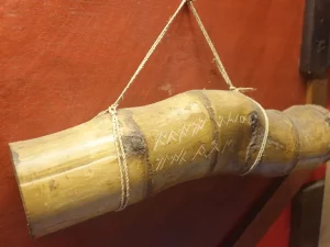 Tabung bambu bergores aksara Ulu digantung dengan tali di depan dinding merah