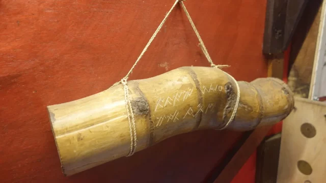 Tabung bambu bergores aksara Ulu digantung dengan tali di depan dinding merah
