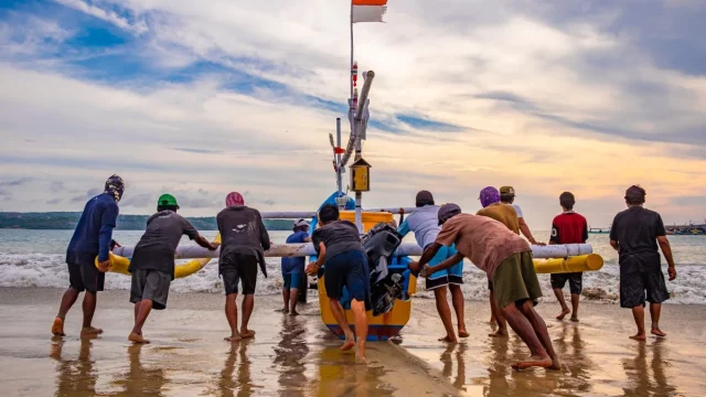 Sekelompok nelayan mendorong perahu bercadik ke laut di Pantai Kedonganan, Bali