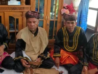 Empat pemangku adat Kerinci berbaju hitam bersulam emas dan berkuluk duduk bersila di rumah adat