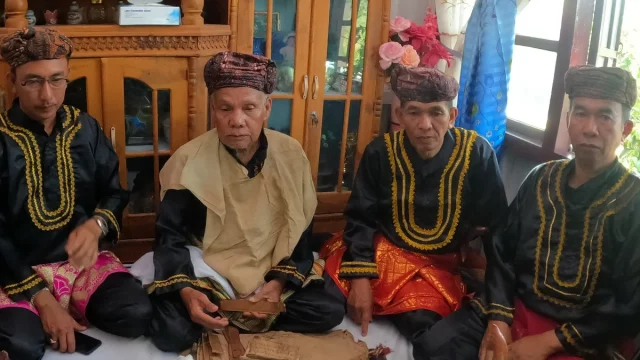 Empat pemangku adat Kerinci berbaju hitam bersulam emas dan berkuluk duduk bersila di rumah adat