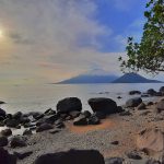 Pantai berbatu di Tidore dengan siluet Gunung Gamalama di Pulau Ternate di kejauhan.