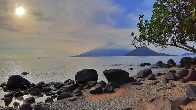 Pantai berbatu di Tidore dengan siluet Gunung Gamalama di Pulau Ternate di kejauhan.