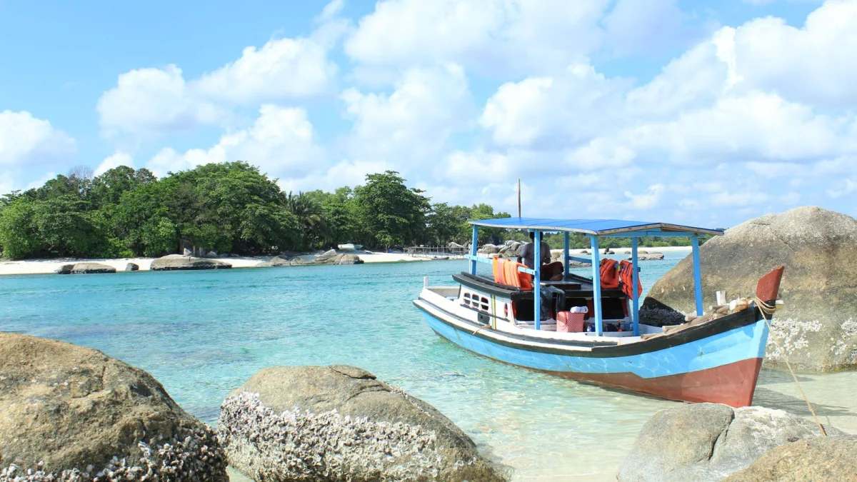 Perahu kayu biru bertambat di antara batu granit Pantai Penyabong, Membalong, Belitung