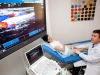 Seorang dokter melakukan pemeriksaan ultrasonografi Doppler pada pasien, dengan citra aliran darah berwarna tampil di layar besar