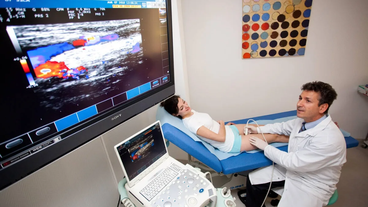 Seorang dokter melakukan pemeriksaan ultrasonografi Doppler pada pasien, dengan citra aliran darah berwarna tampil di layar besar