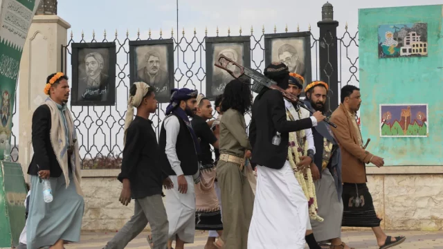 Pendukung Houthi berjalan di Sanaa, Yaman, dengan poster ilmuwan Iran yang tewas dalam serangan Israel di latar belakang.