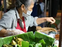 Pedagang lansia menata jajanan berdaun pisang di pasar malam Chon Buri, Thailand