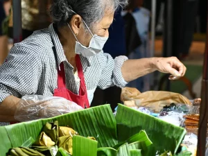 Pedagang lansia menata jajanan berdaun pisang di pasar malam Chon Buri, Thailand