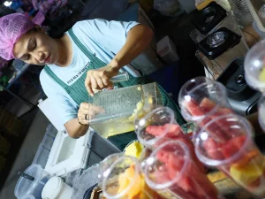 Seorang pedagang menuang potongan buah segar ke blender untuk membuat smoothie di lapak pasar di Thailand.