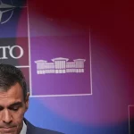 Pedro Sanchez menunduk di depan papan latar belakang berlogo NATO