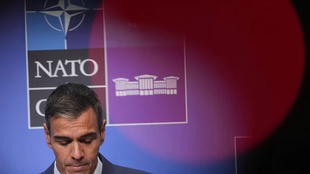 Pedro Sanchez menunduk di depan papan latar belakang berlogo NATO