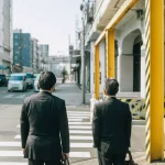 Dua pekerja kantoran pria berjas gelap bersiap menyeberang zebra cross di jalan kota Jepang