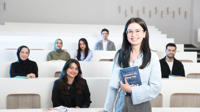 Ilustrasi seorang perempuan berdiri memegang buku di ruang kuliah bertingkat sementara sejumlah mahasiswa duduk di kursi di belakangnya.