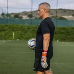 Seorang pelatih memegang bola sepak di lapangan latihan berumput