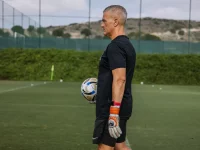 Seorang pelatih memegang bola sepak di lapangan latihan berumput