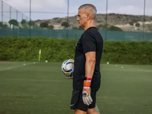Seorang pelatih memegang bola sepak di lapangan latihan berumput