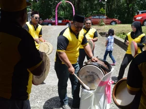 Beberapa laki-laki berseragam kuning hitam memukul kompang dan sebuah bass drum di jalan